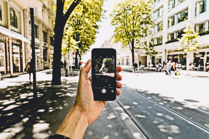 Hand mit Smartphone in einer sonnigen Straße